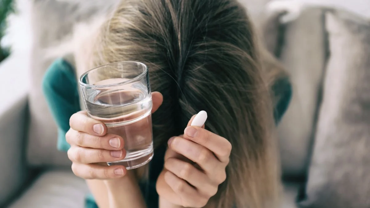 Egy fiatal nő kezében vízzel és antidepresszánssal, fejét a kezébe temeti.