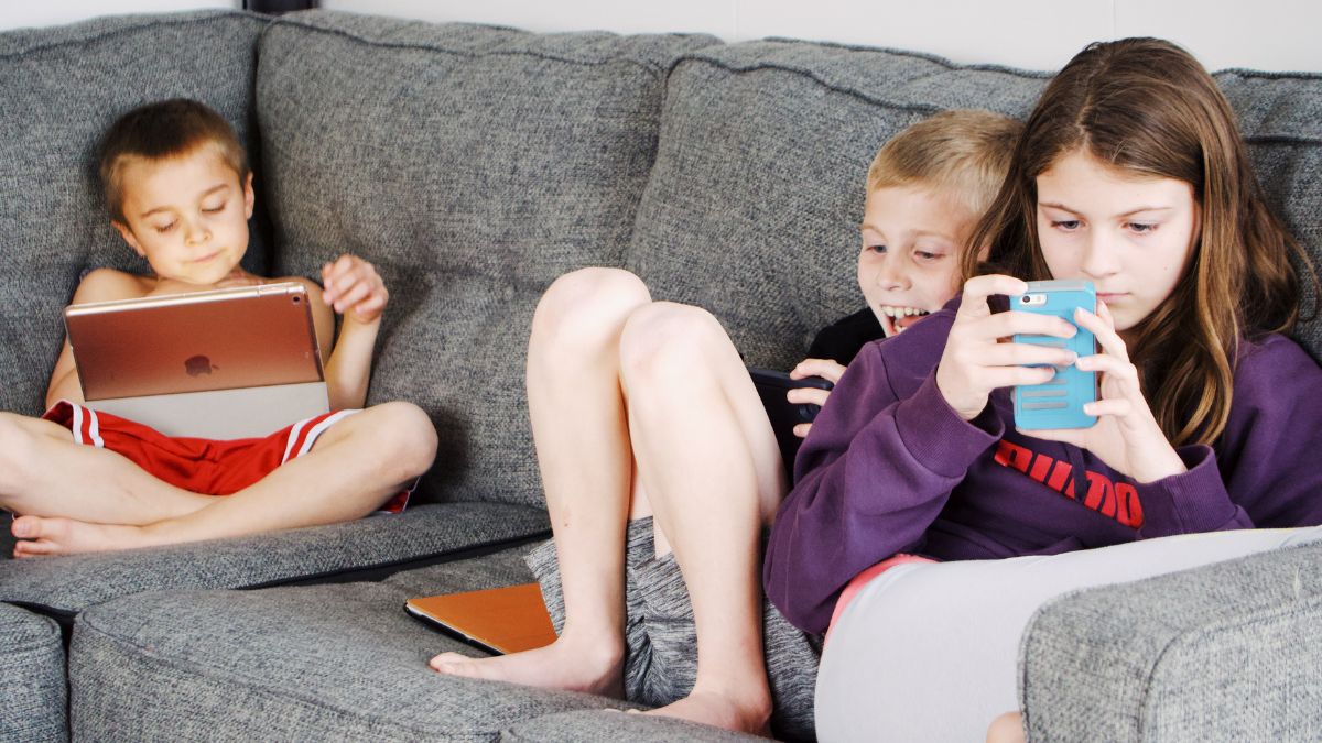 Három gyerek ül egy kanapén, digitális eszközöket használva.