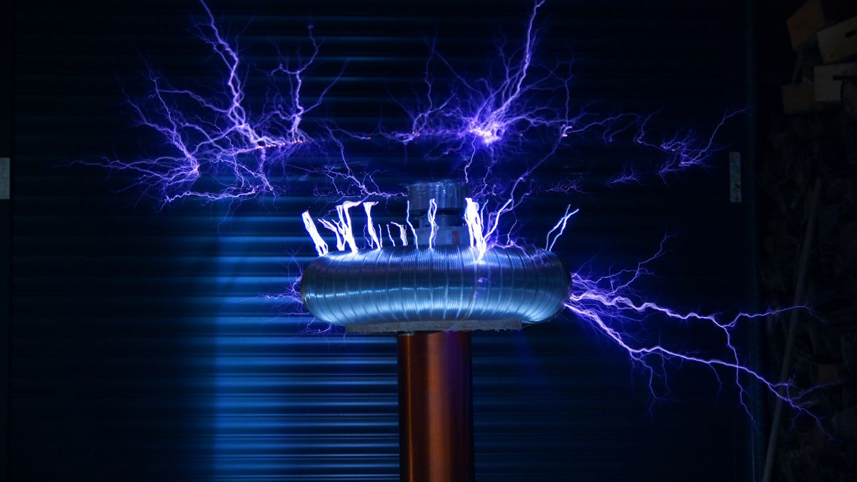 Egy Tesla tekercs, amelyből elektromos ívek és szikrák származnak, sötét háttér előtt.