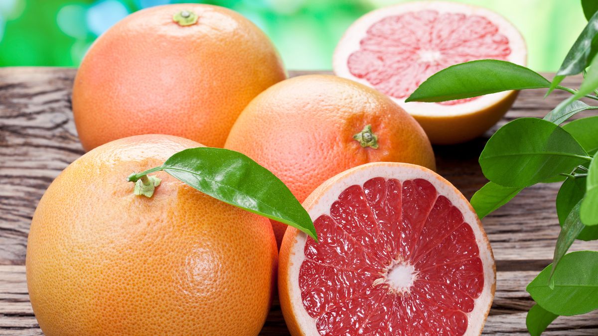 Friss grapefruitok, egy egész és egy fél, zöld levéllel, fából készült felületen.