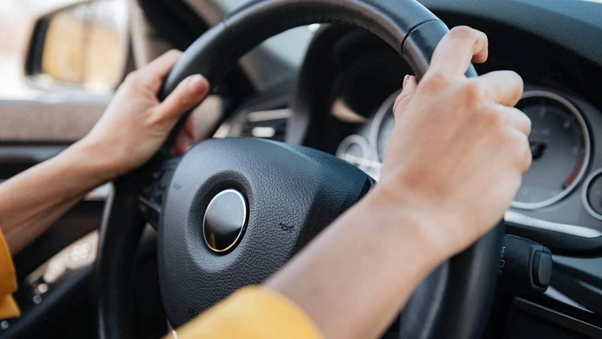 Két kéz fogja a kormányt, amely az ipari automatizálásban használt gyorskormányra utal.