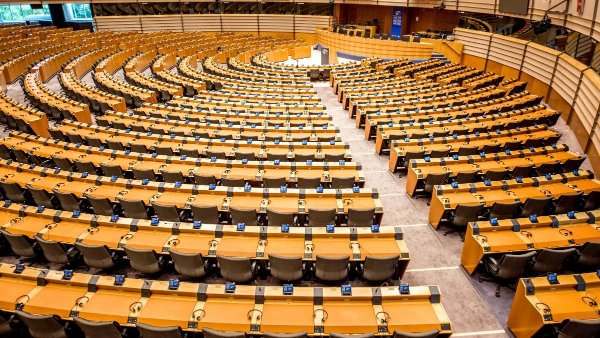 Üres parlamenti ülésterem, sorokban elhelyezett asztalokkal és székekkel.