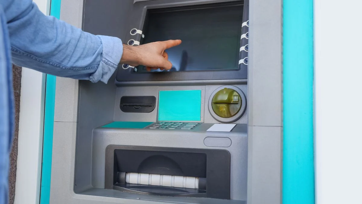 Egy személy mutat a bankautomata érintőképernyőjére, készülve a tranzakcióra.