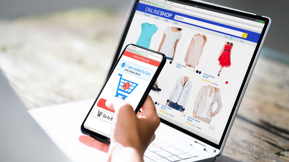 Egy kéz okostelefonon online vásárlást végez, miközben laptopon is termékeket néz.