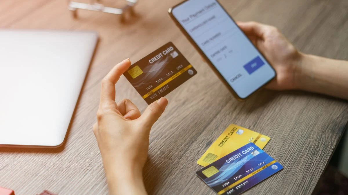 Kézben tartott bankkártya és mobiltelefon, online tranzakcióhoz készülve.