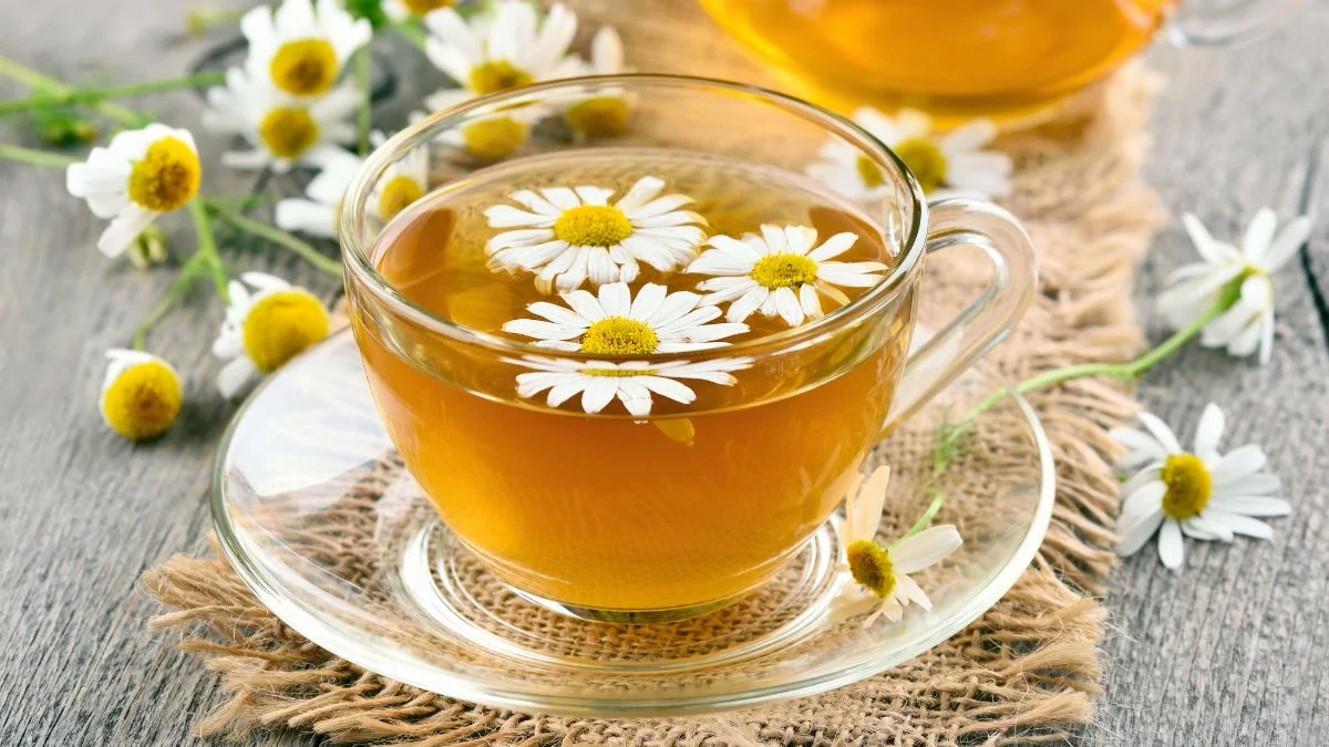 Egy átlátszó pohár kamillatea, a tetején virágokkal díszítve.