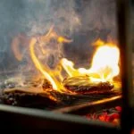 Grillezhető sajtok sülnek a grillen, lángok és füst között.