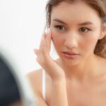 Nő, aki a rozácea tüneteivel küzd a tükör előtt.