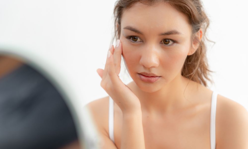 Nő, aki a rozácea tüneteivel küzd a tükör előtt.